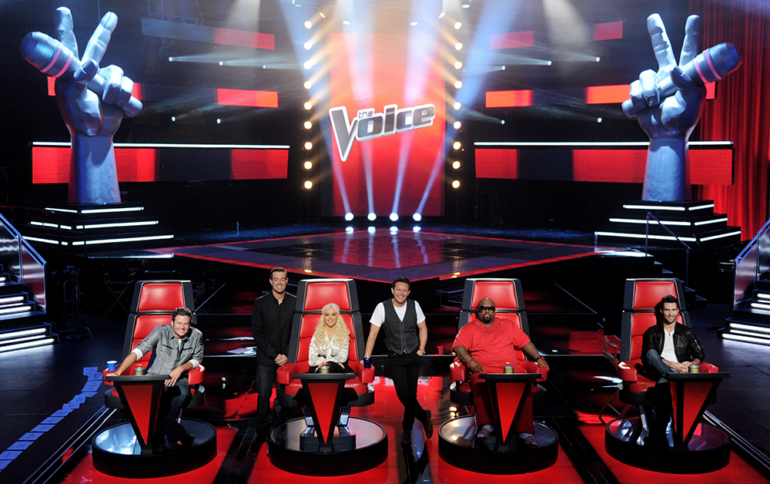 The cast of The Voice USA sitting on the red chairs in the studio