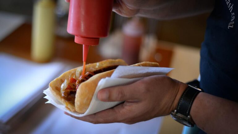 Hand putting sauce on sausage sandwich.