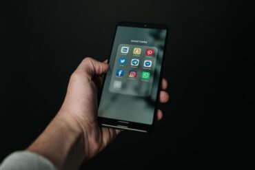 Hand holding a mobile phone with social media app icons displayed.
