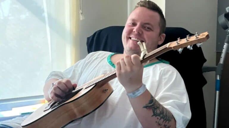 Jake in hospital gown holding a guitar.