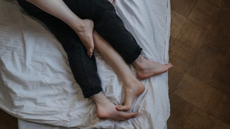 Two sets of legs intertwined in a bed